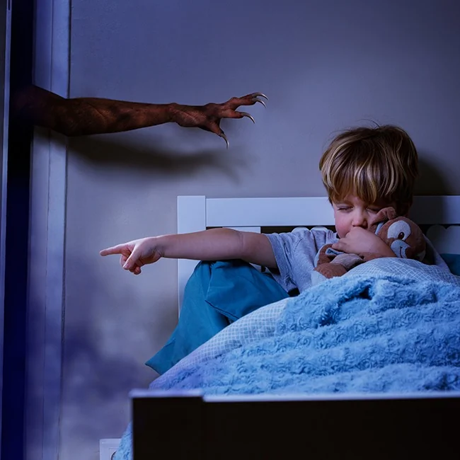 A monster’s hand with claws is trying to reach a boy in a bed, who is holding a plush toy and pointing his finger for it to go away