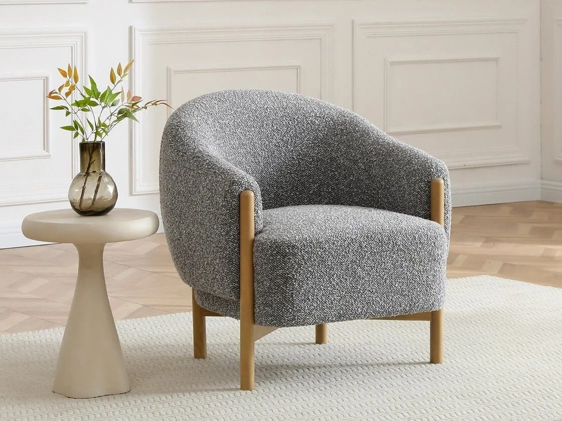 Kyoto Suzie barrel armchair with chunky bouclé upholstery  sloping arms  light wood accents and wooden legs.